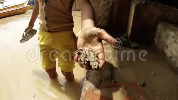 小印度男孩手里拿着泥巴洗着拖鞋把椰子从脏水里扔出来把牛船扔到码头上视频的预览图