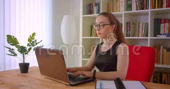年轻漂亮的红头发女商人戴着眼镜手提电脑在办公室里体贴入微在室内视频的预览图