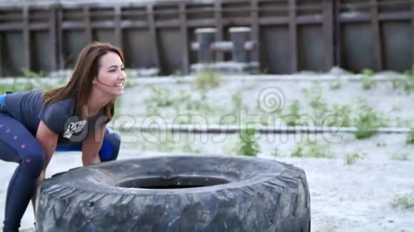 一位年轻的运动女性使用一个大型重型拖拉机轮进行运动训练她的肌肉扔了它关于视频的预览图