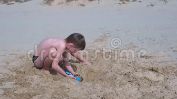 小男孩在沙滩上玩挖铲子试图建造沙塔视频的预览图