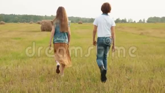 十几岁的男孩和女孩在干草堆背景下的收割场上散步后景男孩女孩走着视频的预览图