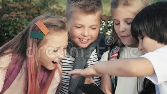 四个快乐的孩子坐在户外用手机微笑视频的预览图