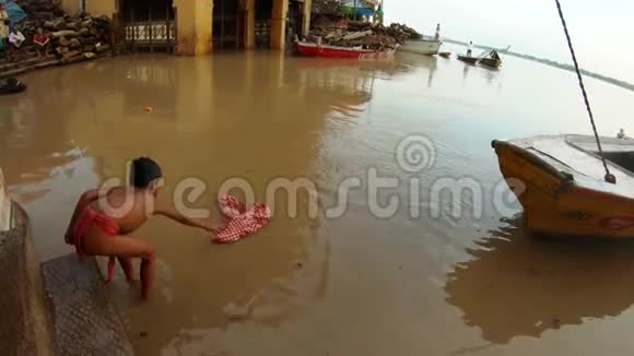 印度儿童在肮脏的水中洗干净的红色物质洪水圣河恒河船上和楼梯上成堆的紫檀木马尼卡尼视频的预览图