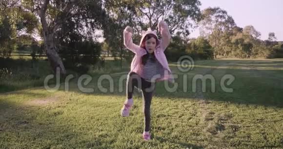 穿着粉红色连帽衫的年轻女孩练习忍者动作忍者并试图在下午的公园里摆出一个姿势金色的光芒视频的预览图