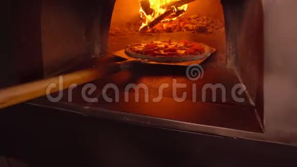 厨师把比萨饼放在烤箱里放在烹饪铁锹上背景中在烤箱里烧木头的概念视频的预览图