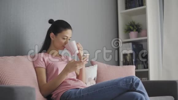 年轻女性在清晨使用带有触摸屏的智能手机和喝咖啡视频的预览图