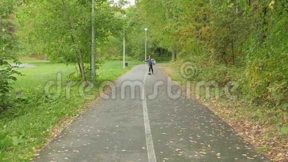 在夏季公园的小路上骑着长板秋天公园小男孩在滑板上玩滑板视频的预览图
