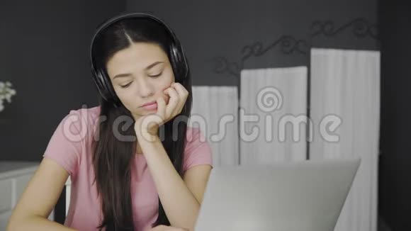 戴着耳机的美女坐在卧室里听着笔记本电脑里的音乐视频的预览图