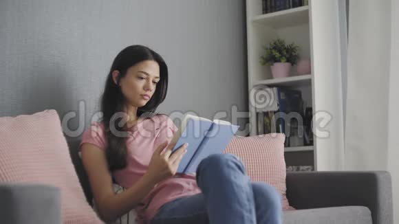 美丽的年轻女子坐在沙发上看一本悲伤的书视频的预览图