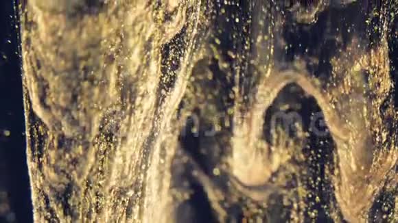 金色的墨水颗粒在水中流动就像黑色背景上五颜六色的混乱一样视频的预览图