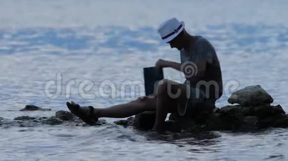 黄昏时分一个人拿着笔记本坐在海边的岩石上从事自然研究的自由职业者希普斯特准备好皮奇视频的预览图