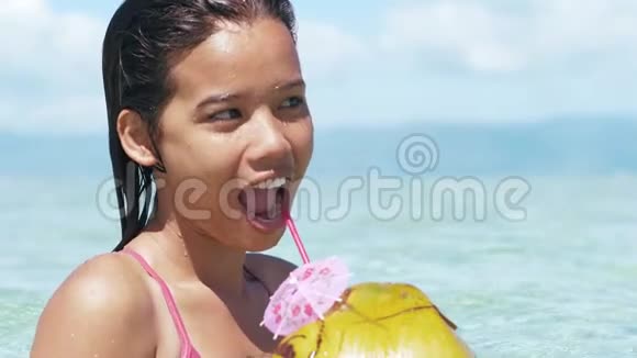 穿着泳装的漂亮亚洲女孩的特写镜头在海边喝椰子视频的预览图