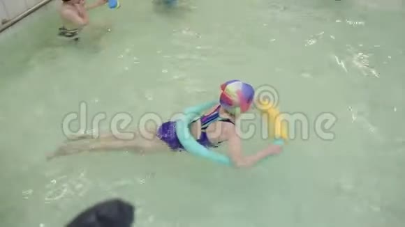 女孩学会在游泳池里游泳一个穿着泳衣的女孩在幼儿园的室内游泳池里游泳视频的预览图