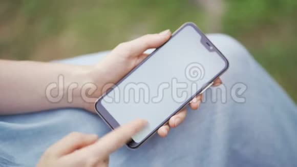 一个女孩在公园里使用她的智能手机浏览社交网络观看新闻视频的预览图