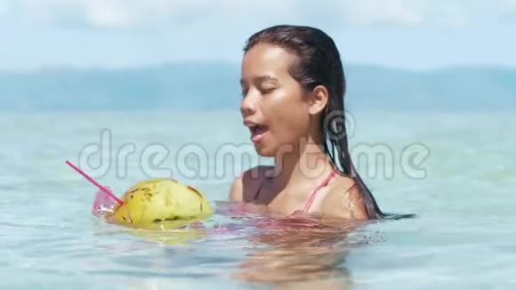 在岛上的一个放松的假期里一个快乐的女人喝椰子的近镜头视频的预览图