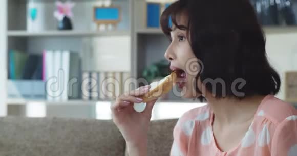 年轻漂亮的女人一边看电视一边吃三明治和牛奶视频的预览图