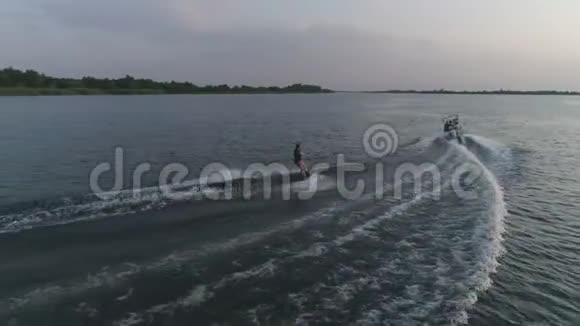 冲浪者在尾板上与朋友一起乘坐摩托艇沿着河流从上面看水视频的预览图