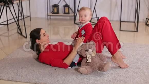 可爱的妈妈和她的小儿子在地毯上躺在房子的地板上玩视频的预览图