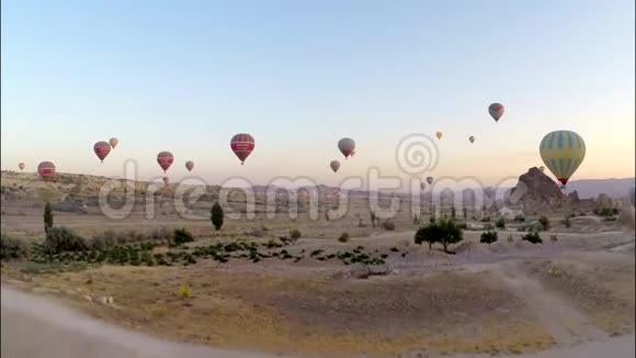 壮观的空中全景看到巨大的热气球在傍晚日落的天空中高高飞翔在岩石沙石和沙漠上视频的预览图