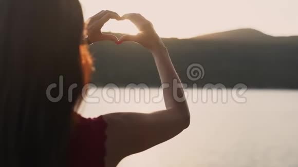 靠近女人的手在背景上随着日落而形成心形动作缓慢视频的预览图