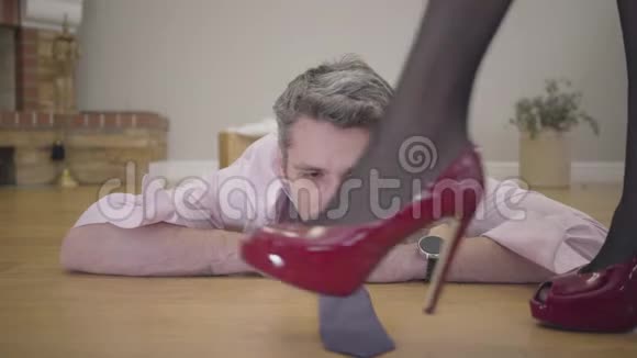 讨厌的丈夫或男朋友躺在地板上的肖像穿红色高跟鞋的漂亮女腿视频的预览图