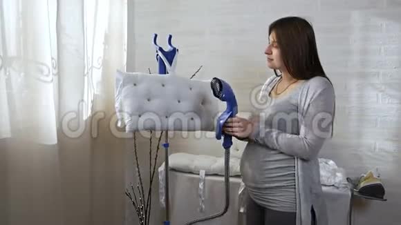 美丽的年轻孕妇穿着灰色西装用蒸汽系统熨烫衣服用她做枕头家庭视频的预览图