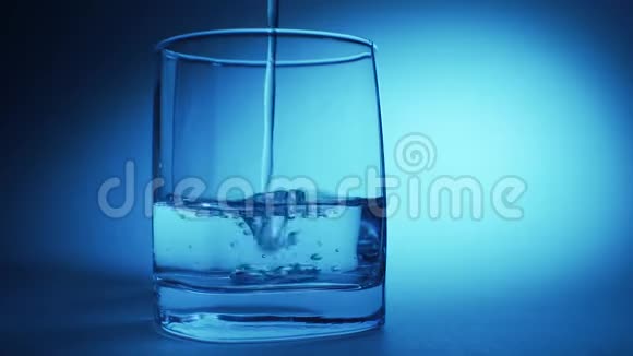在蓝色背景下将水倒入透明玻璃的工作室拍摄视频的预览图