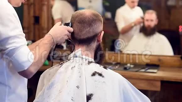 年轻的理发师用修剪器和刷子理发客户坐在镜子前有模糊的倒影视频的预览图