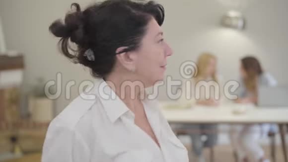 高白种人黑发女人的肖像棕色的眼睛站在家里穿着白色衣服的成熟女士视频的预览图