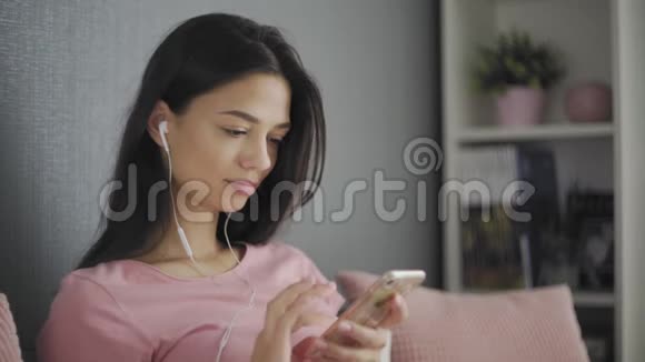 年轻时尚的女士戴着耳机听音乐在家里用手机浏览视频的预览图