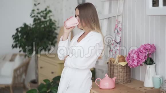 穿着浴袍的年轻女子独自在厨房喝茶享受清晨时光做梦视频的预览图
