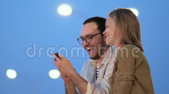 年轻夫妇晚上在智能手机上看照片笑了视频的预览图