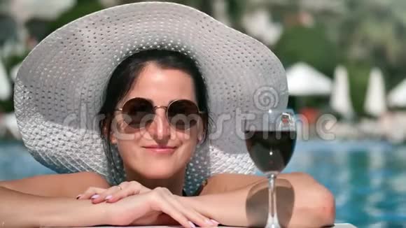 在游泳池享受暑假期间一位身材矮小的女游客微笑着摆着红酒视频的预览图