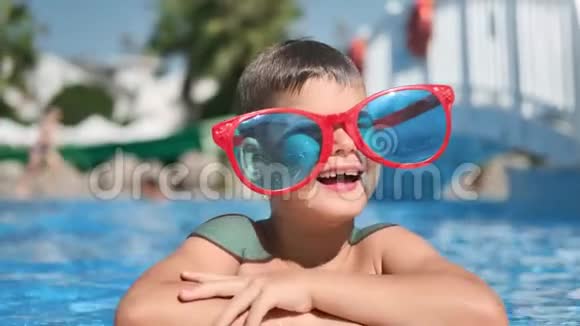 有趣的小男孩戴着大眼镜在游泳池里笑着摆姿势享受夏天的旅行视频的预览图