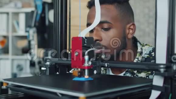 微笑的年轻人看着3D打印机在办公室打印塑料模型视频的预览图