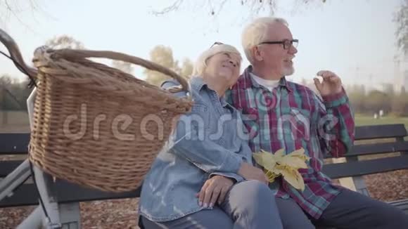 侧面看白种人退休的男人和女人坐在长凳上在阳光下交谈成熟的欧洲家庭或视频的预览图