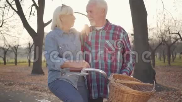 成熟积极的高加索家庭站在阳光下骑着自行车和交谈的秋天公园微笑的退休老人视频的预览图