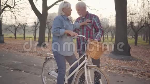 高加索人帮助他可爱的漂亮妻子坐在自行车上积极的欧洲家庭在户外休息视频的预览图