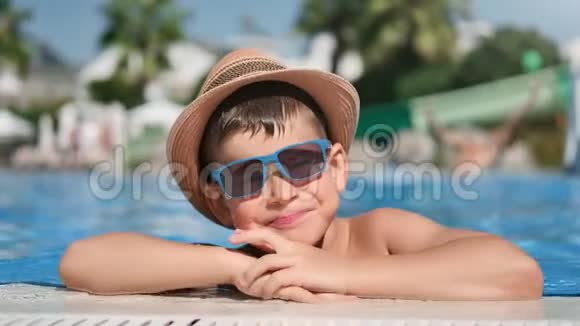快乐男孩戴着太阳镜和帽子在游泳池里摆姿势玩得开心的特写镜头视频的预览图