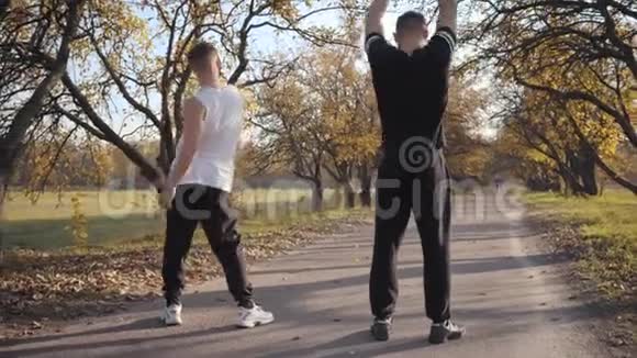 两名白人运动员在秋季公园的后景强壮的成年男孩在锻炼前伸展身体视频的预览图