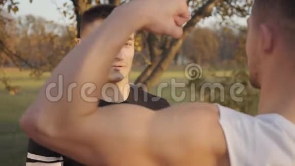 一位年轻的白人运动员在秋天公园的阳光下炫耀自己的肌肉年轻的健美运动员视频的预览图
