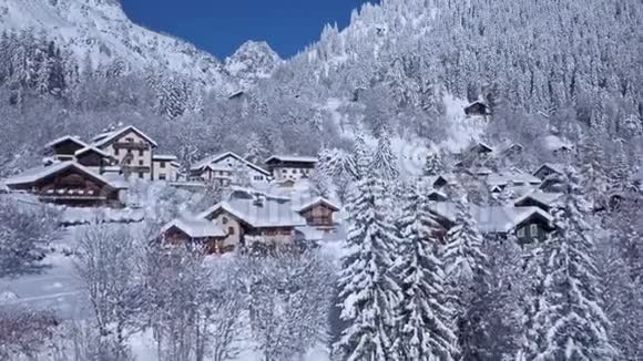 阿尔卑斯山脉冬季森林中一座舒适的豪华小别墅白雪覆盖的屋顶上令人印象深刻的无人机景视频的预览图