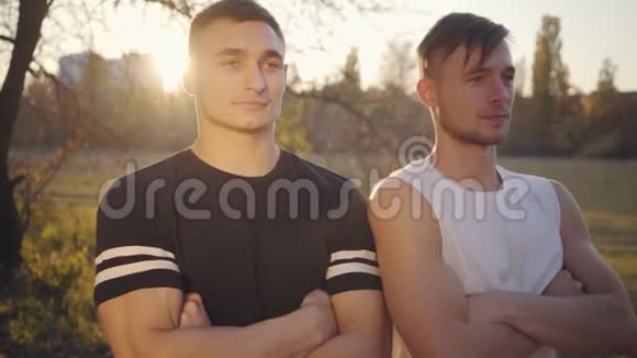 两个年轻的白种人健美运动员站在阳光下看着远处英俊强壮的运动员视频的预览图