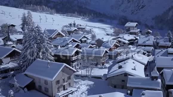 在阳光明媚的冬日空中白天阿尔卑斯山脉白雪覆盖的村庄里一幢幢温馨舒适的小别墅视频的预览图