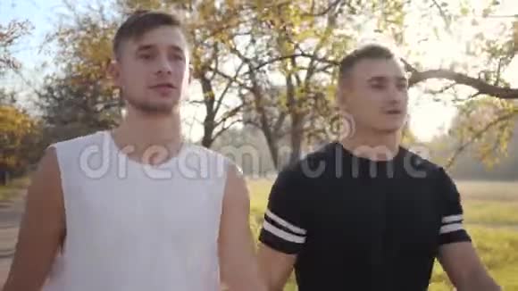 在秋天公园里两个穿着运动服的白种人成年男孩沿着小巷散步做准备的人视频的预览图