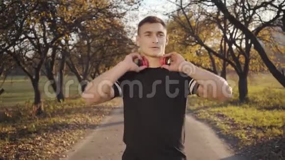 穿着黑色运动服戴着耳机在秋季公园开始跳绳锻炼的白人帅哥视频的预览图