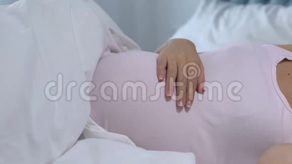 美丽的孕妇躺在床上抚摸着肚子等待着婴儿爱视频的预览图