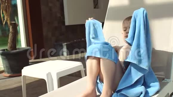 一个裹着毛巾的小男孩坐在游泳池旁的休息室里暖和起来视频的预览图