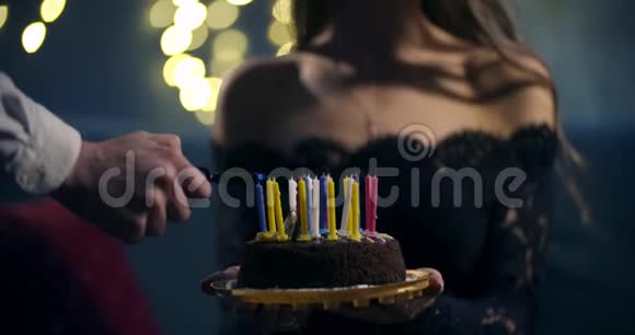性感的女孩穿着一件漂亮的黑色连衣裙手里拿着一个蛋糕一个男人在生日蛋糕上点燃蜡烛概念视频的预览图