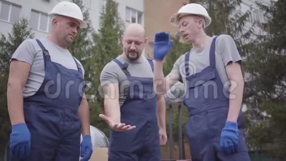 三个肌肉发达的白种人搬运工互相动手开始工作穿蓝色制服带包裹的工人视频的预览图